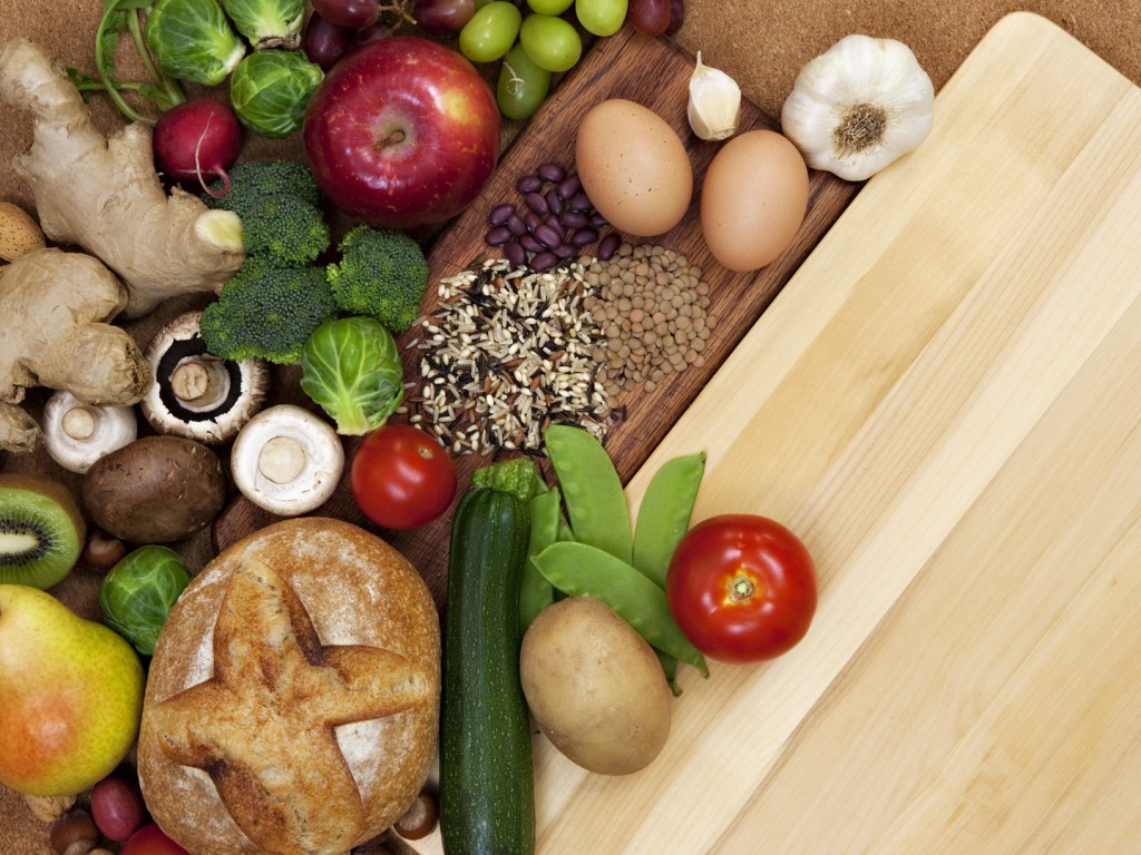 Variety of fresh and healthy food, fruits, vegetables composed around a cutting board.